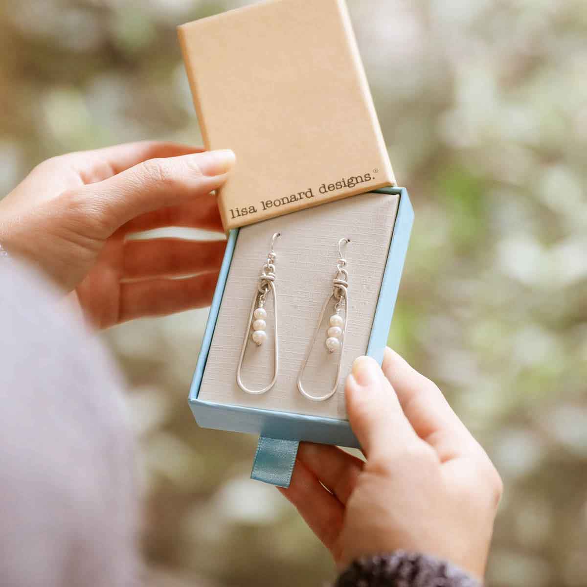 girl holding a mother's love sterling silver pearl earrings in a lisa leonard box