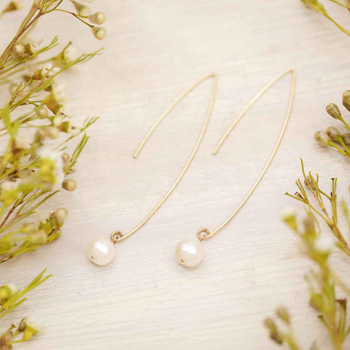 10k yellow gold artisan pearl earrings on a wood background with floral
