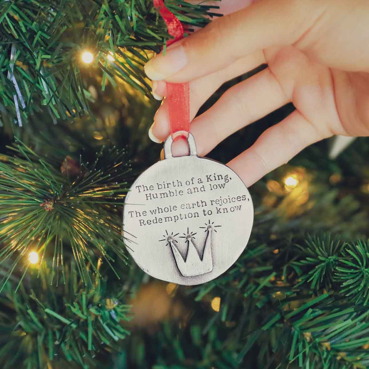 handcrafted babe in a manger pewter ornament set hung on sheer red ribbon stamped with a Christmas story poem on Christmas tree