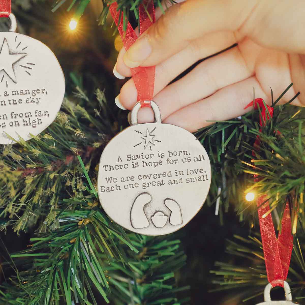 handcrafted babe in a manger pewter ornament set hung on sheer red ribbon stamped with a Christmas story poem on Christmas tree