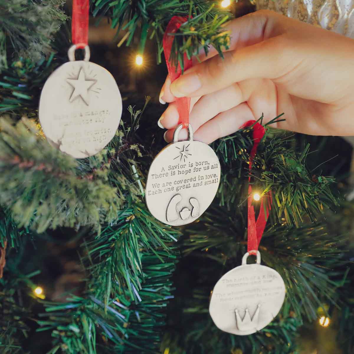 handcrafted babe in a manger pewter ornament set hung on sheer red ribbon stamped with a Christmas story poem on Christmas tree