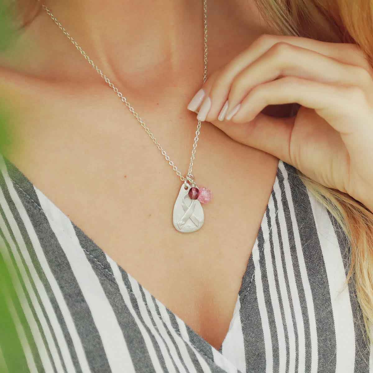 Cancer awareness necklace handcrafted in sterling silver with a matte brushed finish and hung next to a rose quartz and crystal bead