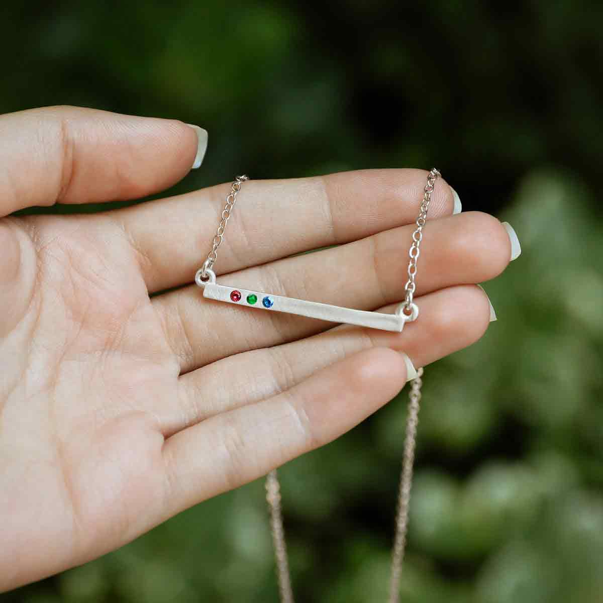 hand holding sterling silver cross bar birthstone necklace strung on a link chain customizable with up to 7 genuine 2mm birthstones