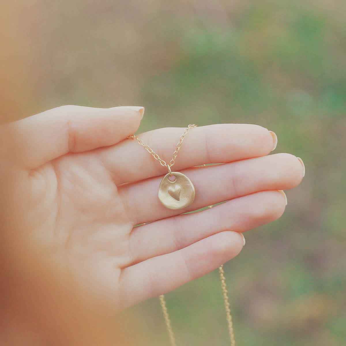 girl's hand holding 10k yellow gold full of love necklace strung on gold-filled link chain