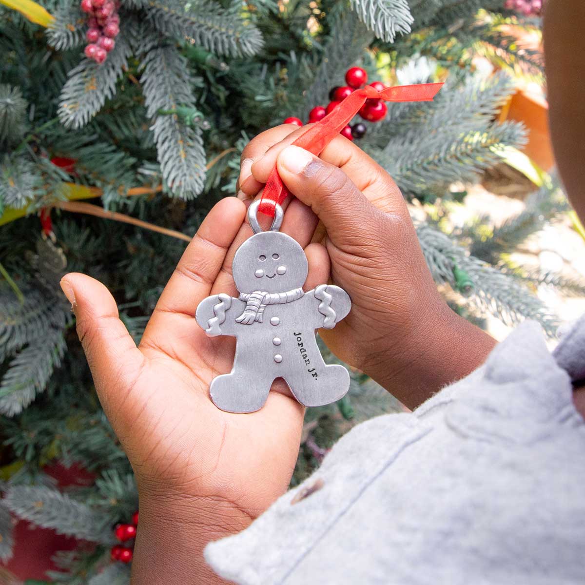 Gingerbread boy ornament hand-molded and cast in fine pewter hung from a sheer red ribbon with a personalized word being placed on Christmas tree