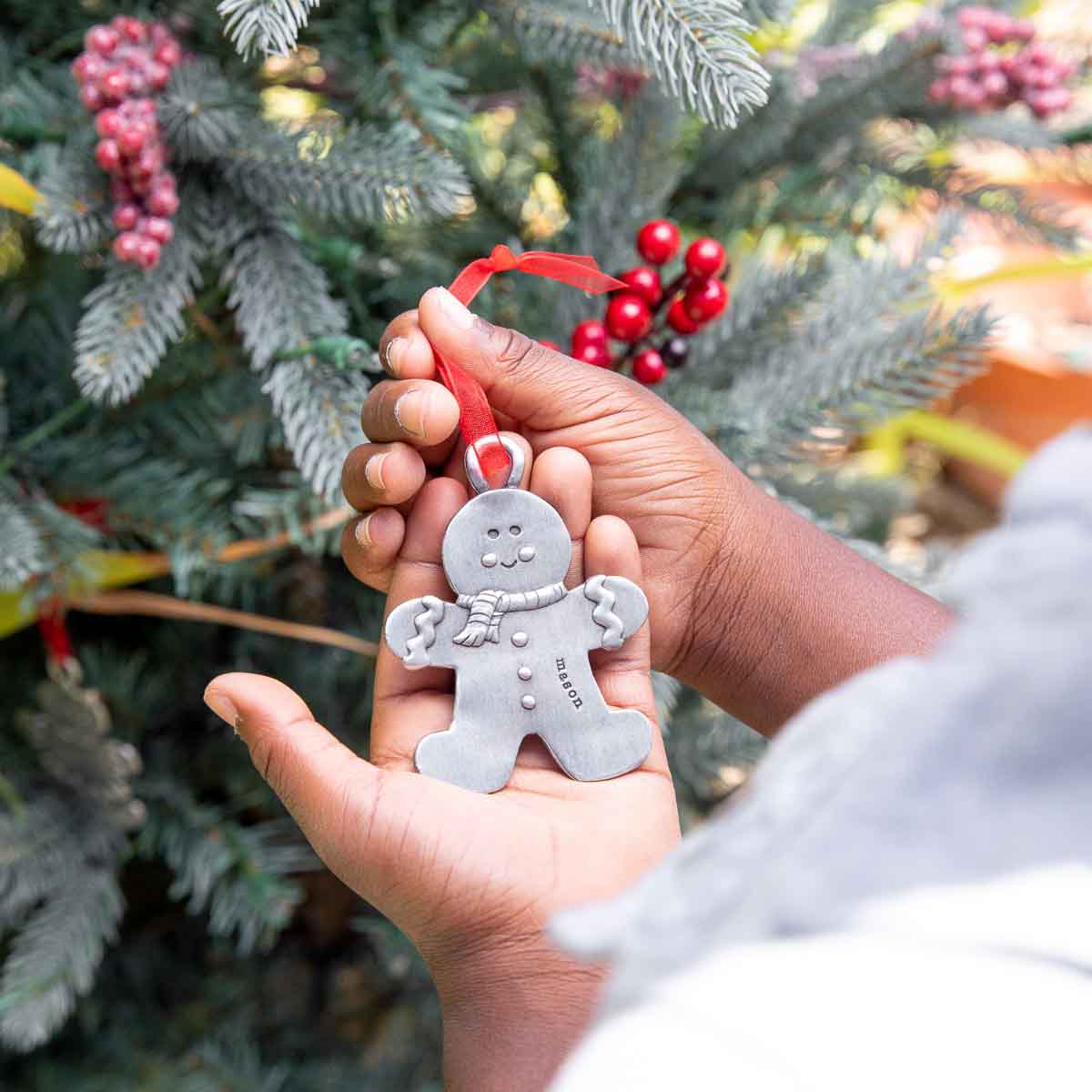 Gingerbread boy ornament hand-molded and cast in fine pewter hung from a sheer red ribbon with a personalized word being placed on Christmas tree