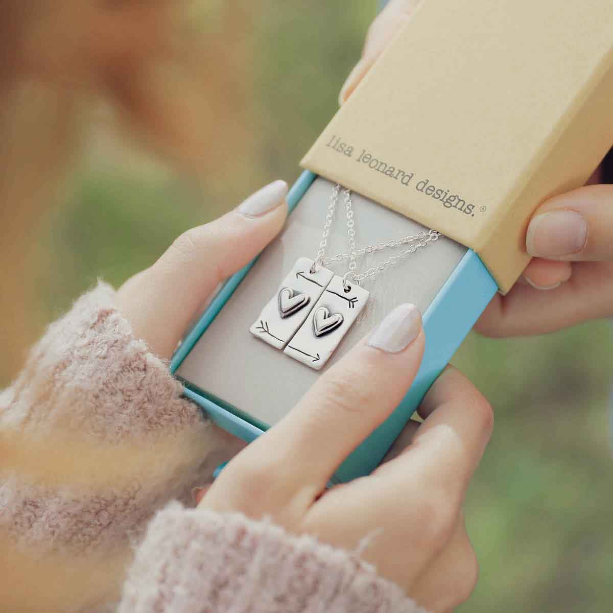 girl giving another girl the sterling silver i love you necklace set in a lisa leonard box