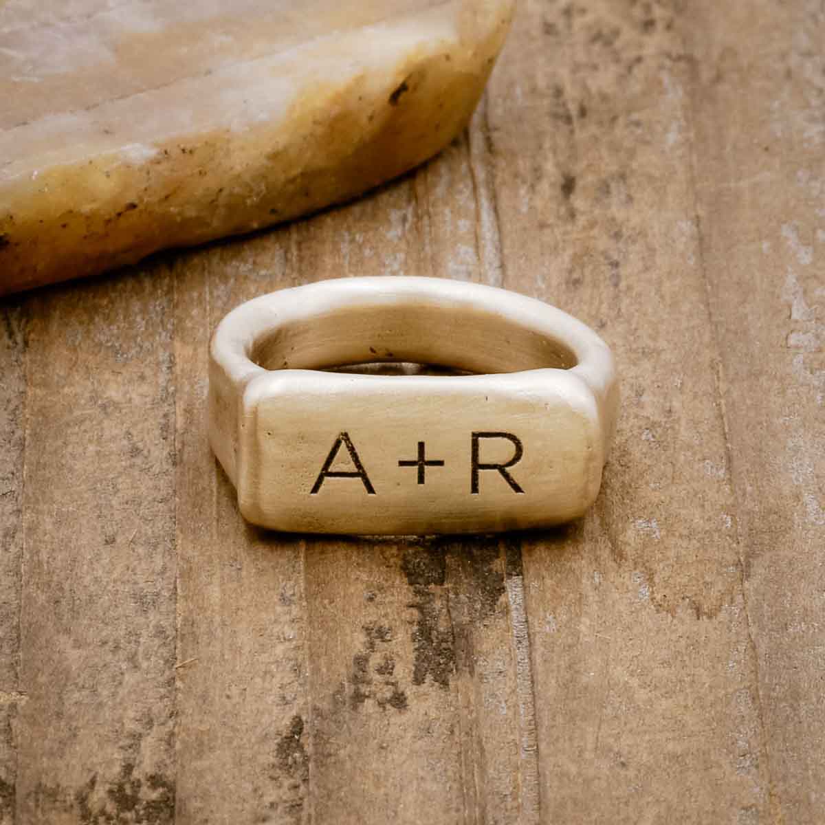 a 10k yellow gold Make Your Mark Signet Ring, personalized with monogram, sitting on a wood background