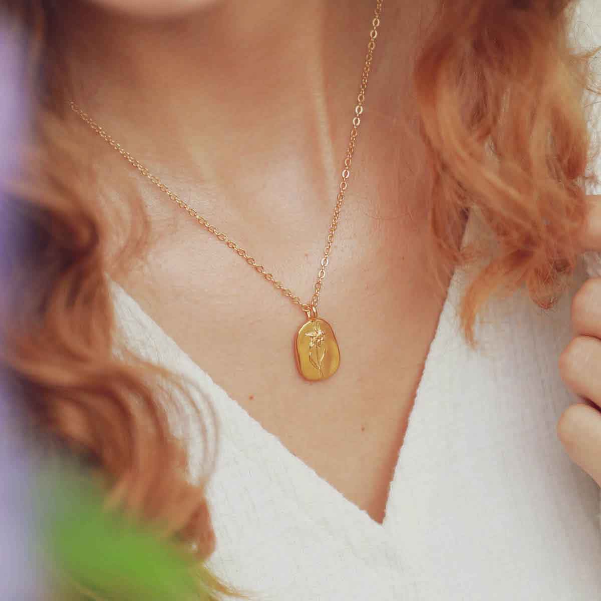 girl holding a gold plated March birth flower necklace with an 18" gold filled link chain