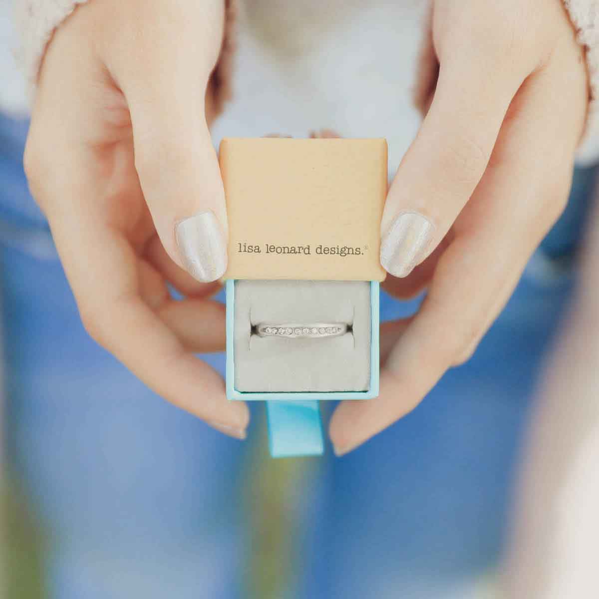 hands holding Passage ring handcrafted in sterling silver and display of 1.5mm cubic zirconias in original packaging