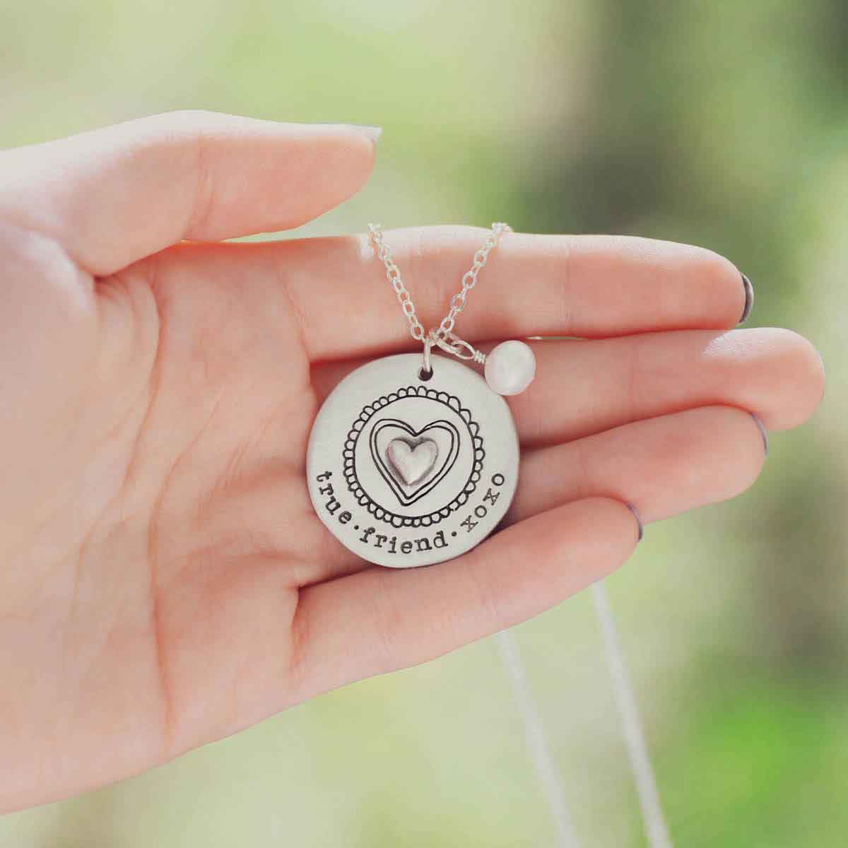 hand holding Personalized sterling silver original brave love necklace with a matte brushed finish and strung on a sliver link chain