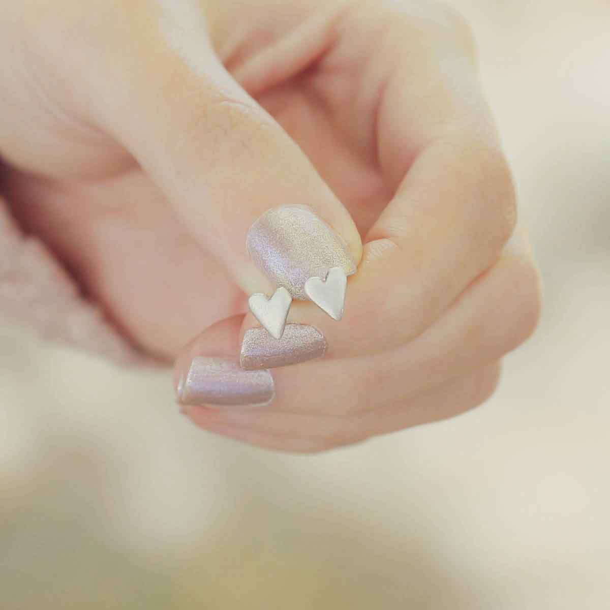 hand holding sterling silver tiny heart stud earrings