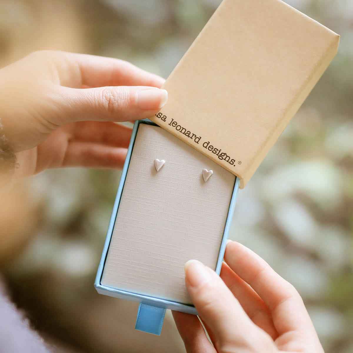 girl holding sterling silver tiny heart stud earrings in a lisa leonard jewelry box