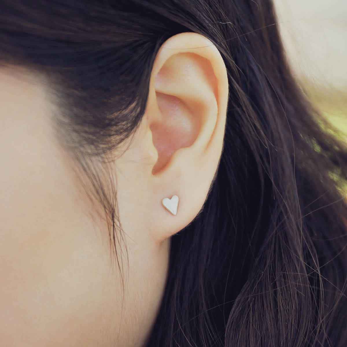 girl wearing sterling silver tiny heart stud earrings with a matte brushed finish