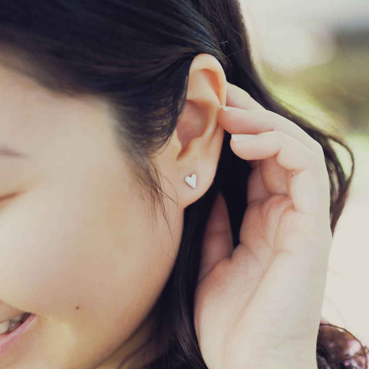 girl wearing sterling silver tiny heart stud earrings with a matte brushed finish