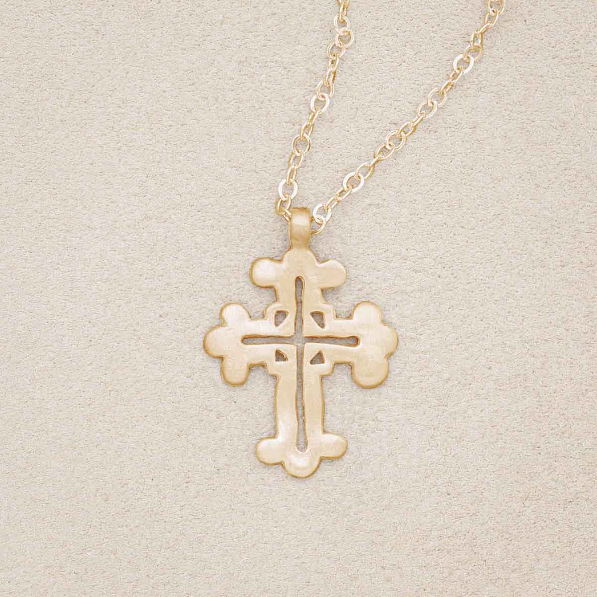 14k yellow gold work of art cross necklace, on beige background