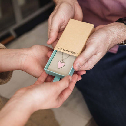 Girl holding her Brave Love heart necklace handcrafted in pewter with choice of color epoxy in original packaging