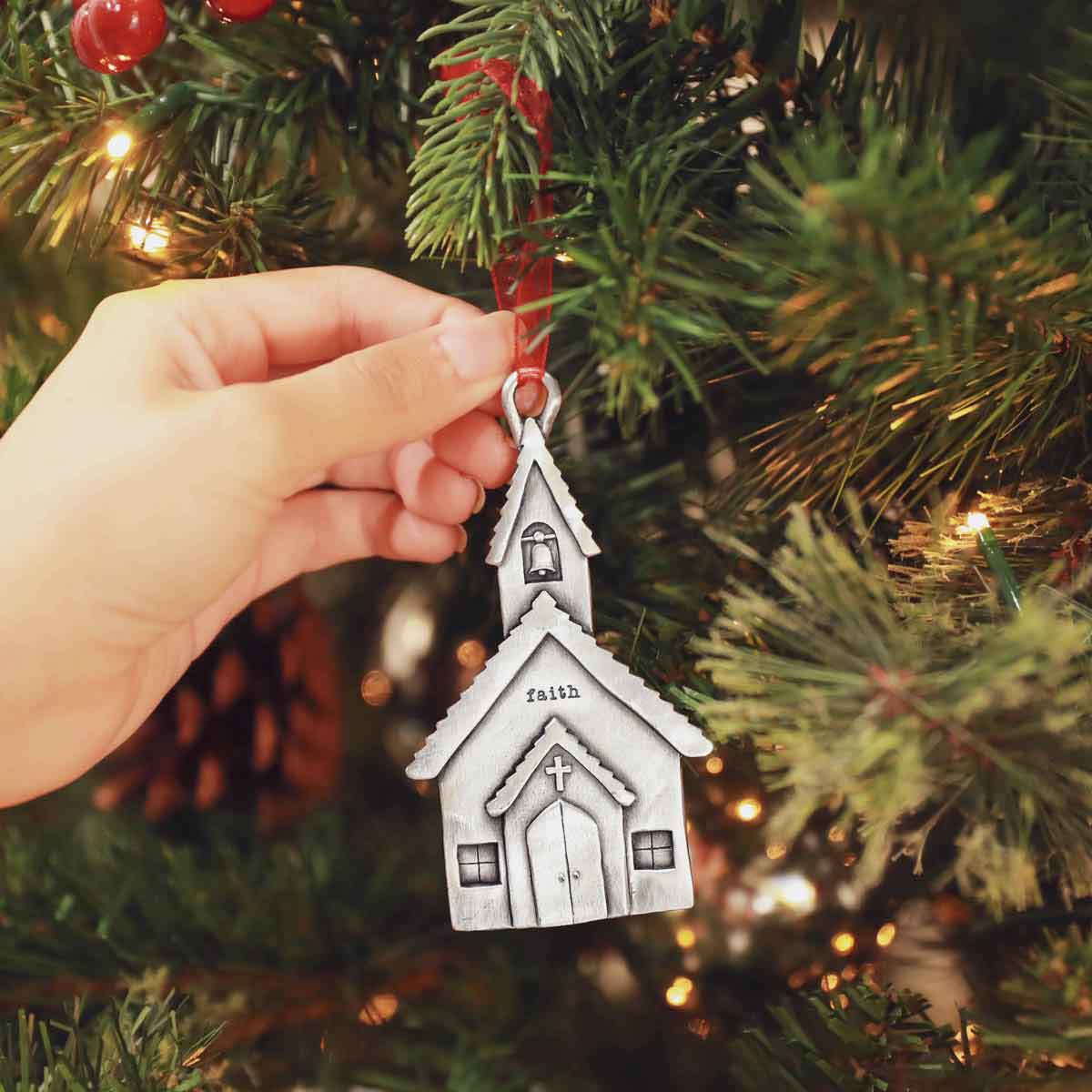 hand hanging a Church Bells Ornament on a Christmas tree