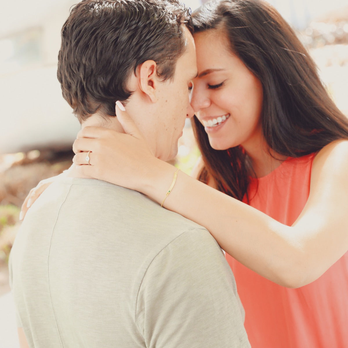 A couple hugging with the woman showing her handcrafted 14k gold cross bar birthstone bracelet 